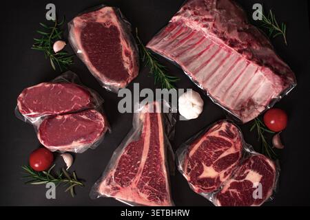 Un colpo top-down professionale con una varietà di tagli di carne cruda di alta qualità, tra cui bistecche e costolette, conservati in confezioni sottovuoto. Il composit Foto Stock