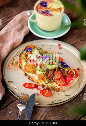 Toast artigianale a lievitazione naturale con falafel, pomodori ciliegini e fiori commestibili, serviti insieme a un latte matcha decorato. Foto Stock