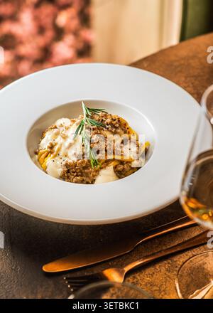 Un piatto di pasta lunga condita con un ricco sugo di carne alla bolognese, condito con formaggio bianco fuso e un rametto di rosmarino fresco. Foto Stock