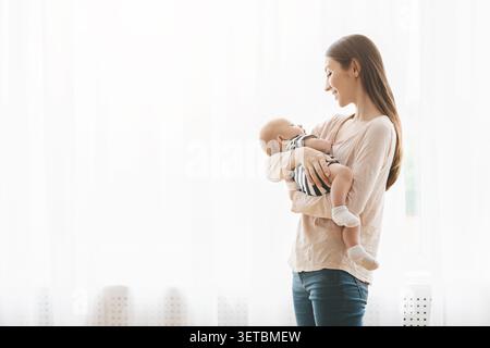 La madre tiene delicatamente il suo bambino in una stanza luminosa e serena durante un pomeriggio di sole Foto Stock