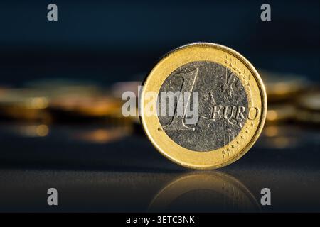 Una moneta in euro su uno sfondo scuro con monete più piccole in un'illuminazione elegante Foto Stock