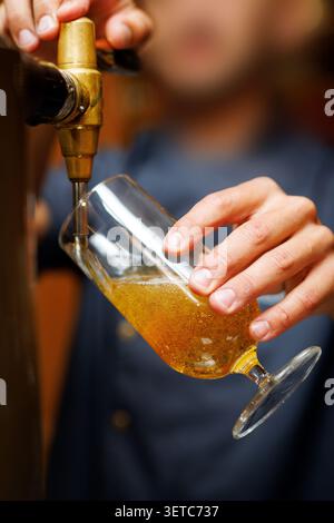 Prima piano di un barista che versa birra fresca alla spina in un bicchiere Foto Stock