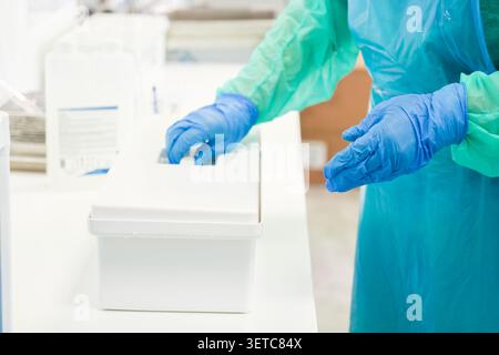 L'operatore sanitario che indossa dispositivi di protezione individuale gestisce le forniture cliniche in un ambiente di laboratorio pulito, sottolineando il protocollo di igienizzazione Foto Stock