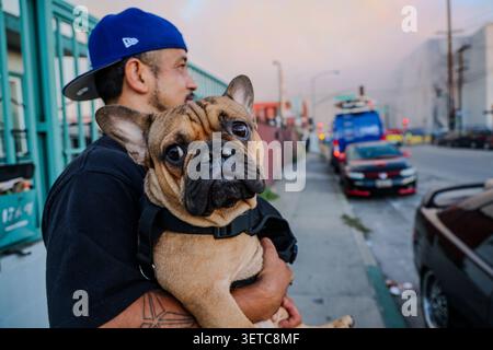 Los Angeles, California, Stati Uniti. 21 giugno 2026. Un uomo che vive proprio accanto al magazzino dei lignaggi in fiamme a Boyle Heights tiene il suo Bull Dog mentre il fumo spessa sale sul quartiere, coprendo i residenti e i loro animali domestici con fumo e fumi. Sullo sfondo è possibile vedere l'acqua dei camion antincendio spruzzata sul gigantesco edificio che si sta fumando. (Immagine di credito: © Amy Katz/ZUMA Press Wire) SOLO PER USO EDITORIALE! Non per USO commerciale! Crediti: ZUMA Press, Inc./Alamy Live News Foto Stock