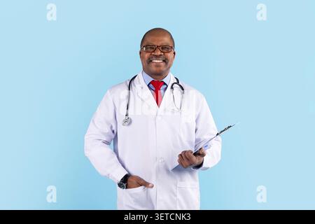 Medico nero sorridente che indossa occhiali, cappotto bianco e stetoscopio che regge gli appunti Foto Stock