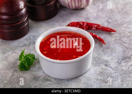 Vivace salsa di peperoncino dolce presentata in ramekin bianco. Condimento rosso brillante, perfetto per la cottura a immersione, con peperoni rossi secchi prezzemolo fresco Foto Stock