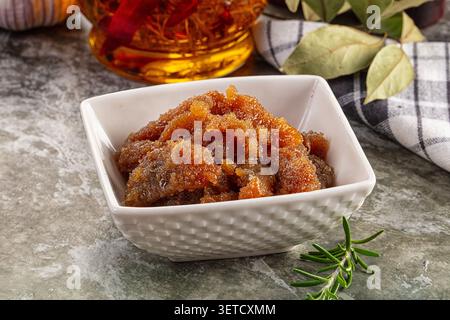 Primo piano di croccanti fritti di maiale in una ciotola di ceramica bianca, accompagnati da un barattolo di olio di peperoncino, foglie di alloro, ramoscello di rosmarino, aglio su sasso testurizzato surfa Foto Stock