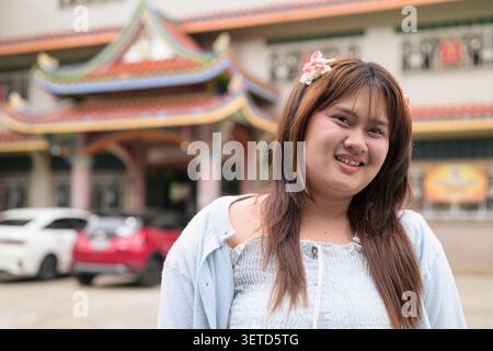 Un ritratto orizzontale ravvicinato di una giovane ragazza isana tailandese del sud-est asiatico che inclina la testa e tocca i capelli con un sorriso dolce. Foto Stock