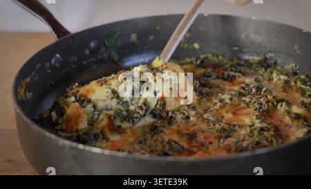 Vista ravvicinata di spinaci cremosi e gratin di porri mescolati in una padella su un bancone della cucina. Foto Stock