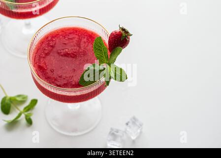 Cocktail rosso con crema di fragole in un bicchiere vintage. Guarnite con foglie di menta fresca e una fragola intera Foto Stock