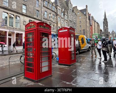 Due iconiche cabine telefoniche rosse sul Royal Mile, High Street, Edimburgo, Scozia. Edifici in pietra e pedoni fiancheggiano la strada bagnata. Foto Stock