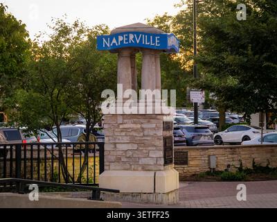 Pietra e pilastro Naperville cartello di benvenuto monumento sul lungofiume con auto parcheggiate e alberi lussureggianti al tramonto in Illinois Foto Stock