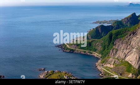 Spettacolare vista aerea di tortuose strade costiere che abbracciano scogliere ripide nelle isole Lofoten, Norvegia. Montagne lussureggianti e verdi si incontrano con il mare blu profondo Foto Stock