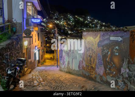 Strada notturna a Cusco, Perù, che sale su una ripida pendenza e murale sul vecchio muro. Foto Stock