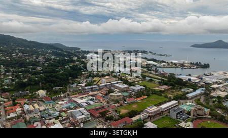 Vista panoramica del porto di Victoria con vari edifici, paesaggi verdi e isole in lontananza sotto un cielo nuvoloso. Seychelles, Mahe. Foto Stock