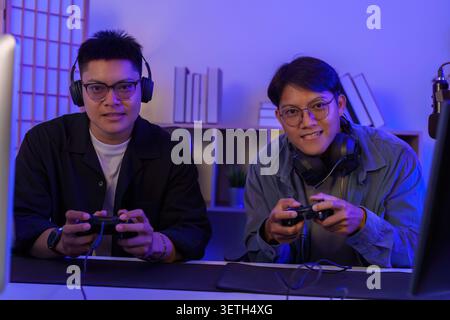 Uomini asiatici giocatori che giocano ai videogame con controller e cuffie per l'intrattenimento con tecnologia eSport Foto Stock