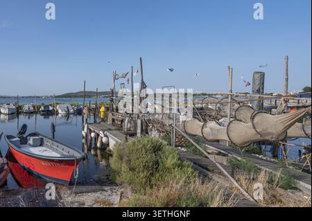Le tradizionali reti a trappola sono appese ad asciugare su passerelle in legno sopra l'acqua calma, mentre una barca da pesca rossa ormeggiava sulla riva contro la vasta ba Foto Stock