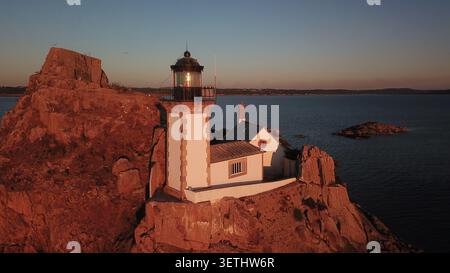 Vista aerea del Phare de l'ile Louet illuminata dalla calda luce dorata del tramonto, arroccata su scogliere rocciose circondate dal mare calmo di Carantec Foto Stock