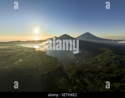 Vista aerea del Lago Batur, del Monte Abang e del Monte Agung all'alba con lussureggiante paesaggio vulcanico e nebbia mattutina a Kintamani, Bali, Indonesia. Foto Stock