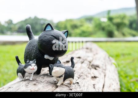 Chiang mai, Tailandia - 19 giugno 2026 : grande statuetta nera di gatto con due piccole statuine nere e bianche su vecchi tronchi intemprati all'aperto Foto Stock