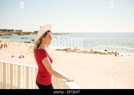 Donna sorridente, guardando l'oceano da un balcone, in un giorno d'estate luminoso Foto Stock