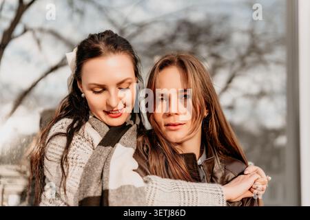 Amici che abbracciano l'autunno due giovani donne condividono un momento tenero indossando maglioni e giacche in pelle alla luce soffusa del sole Foto Stock
