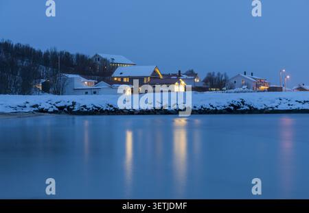 Vista delle case tradizionali ricoperte di neve lungo il lungomare al crepuscolo a Tromso, Troms, Norvegia. Foto Stock