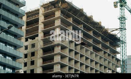 Un grattacielo è attualmente in costruzione, con una struttura in cemento a vista, reti di sicurezza e una gru a torre nelle vicinanze Foto Stock