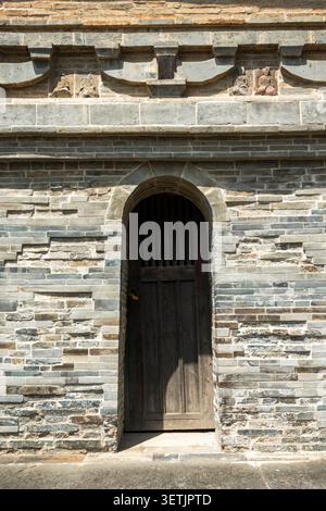 Una porta di legno intemprata posta in un ingresso ad arco in mattoni grigi di un'antica pagoda. Foto Stock