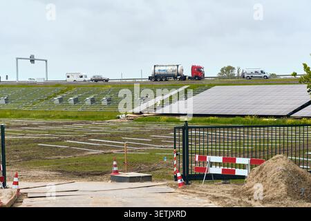 Den Oever, Paesi Bassi - 20 maggio 2026: Vista di un cantiere di un impianto solare lungo l'autostrada A7 con lavoratori che installano pannelli e veicoli di passaggio Foto Stock