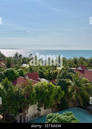 Vista panoramica della costa con tetti rossi del resort e lussureggianti palme. Uno splendido paesaggio tropicale che mostra lo scintillante orizzonte blu dell'oceano dietro a. Foto Stock