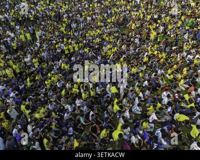 Dacca, Bangladesh - 20 giugno 2026: Veduta aerea di una grande folla di persone sedute sull'erba in un parco pubblico, con maglie colorate e casual cl Foto Stock