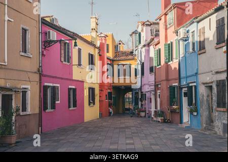 Vicolo vuoto e stretto circondato da case colorate di rosa, giallo e blu in una giornata di sole a Burano, Italia. Foto Stock