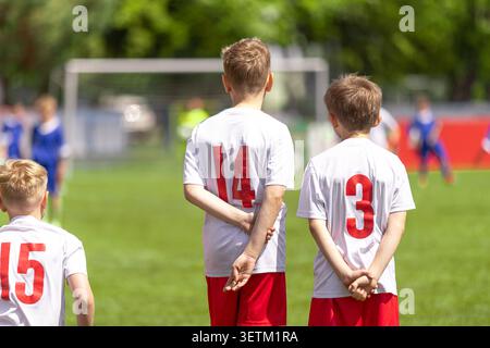 Giovani giocatori di calcio in attesa di Sideline: Bambini in bianco e rosso uniformi guardare la partita Foto Stock