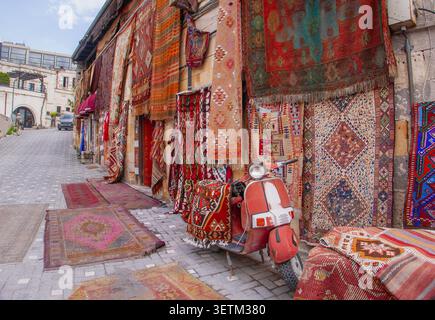 CAPPADOCIA, TURCHIA - 23 APRILE 2026: Una vivace mostra di tappeti e tappeti tradizionali turchi appesi alle pareti di pietra di un negozio, con una vinta Foto Stock