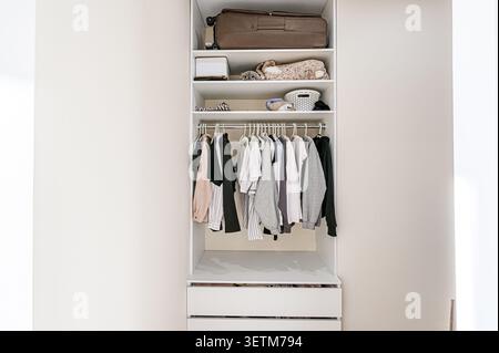 Un guardaroba bianco ben organizzato è pieno di vestiti, bagagli e altri oggetti ordinatamente disposti sugli scaffali e appesi su un'asta. Cassetti al botto Foto Stock