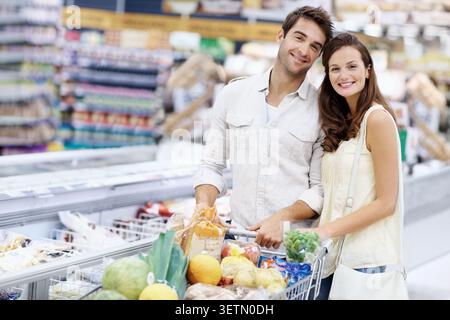 Passeggiare, ritrarre e fare una coppia felice con un carrello nel supermercato, nel fine settimana. Sorridi, incontri e uomo con donna con prodotti Foto Stock