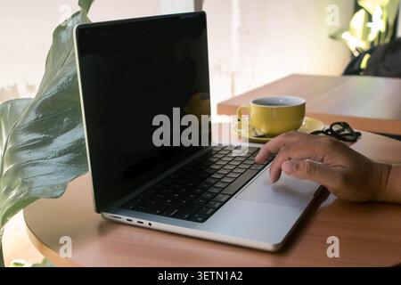 Stile di lavoro remoto con laptop e caffè nell'accogliente caffè, digitazione freelance su computer con mockup a schermo bianco Foto Stock