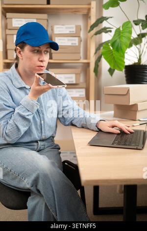 Giovane lavoratrice di e-commerce che invia messaggi vocali in ufficio. Concetto di piccole imprese, pmi ed e-commerce Foto Stock