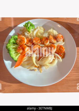 Un piatto di pesce splendidamente placcato con succulenti gamberi grigliati abbinati a vivaci broccoli al vapore, cipolle saltate e carote fresche, tutto eleg Foto Stock