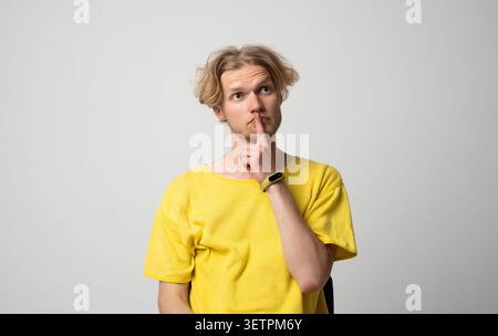 Giovane biondo con una maglietta gialla che riflette o contempla un problema, pensa a soluzioni, prende una decisione o ricorda qualcosa Foto Stock