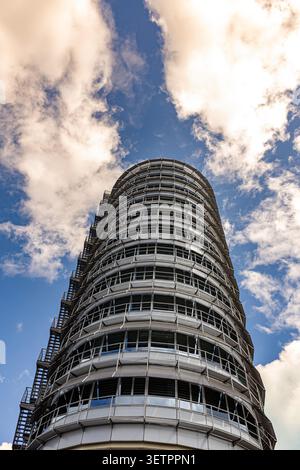 Un grattacielo cilindrico futuristico moderno sullo sfondo di nuvole rosa sorprendenti e di un cielo blu vibrante. Foto Stock