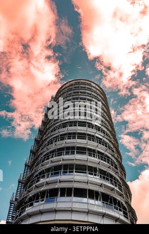 Un grattacielo cilindrico futuristico moderno sullo sfondo di nuvole rosa sorprendenti e di un cielo blu vibrante. Foto Stock