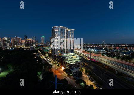 Percorsi leggeri da auto che passano davanti allo skyline illuminato di Dallas, Texas, sull'Interstate 35 subito dopo il tramonto in una notte d'estate limpida. Foto Stock