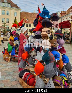 Tallinn, Estonia - 15 agosto 2020: Un venditore di costumi medievali si erge accanto a una colorata esposizione di cappelli in feltro fatti a mano in una bancarella del mercato durante il Talli Foto Stock