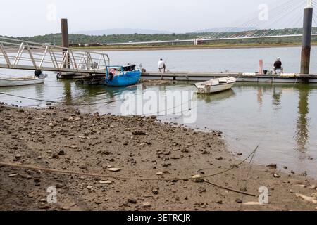Due uomini stanno pescando da un molo mentre piccole barche sono legate al molo, con un ponte moderno sullo sfondo Foto Stock
