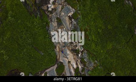 Vista aerea di un scalatore su una formazione rocciosa di granito ricoperta di muschio circondata da una lussureggiante vegetazione verde a Lofoten. Contrasto drammatico tra Foto Stock