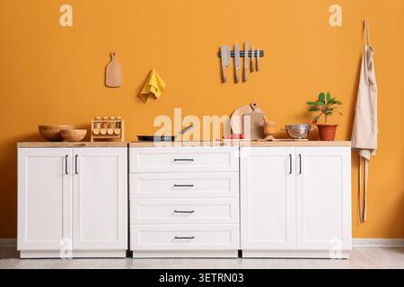 Interni moderni con armadi bianchi e pareti arancioni con utensili da cucina Foto Stock