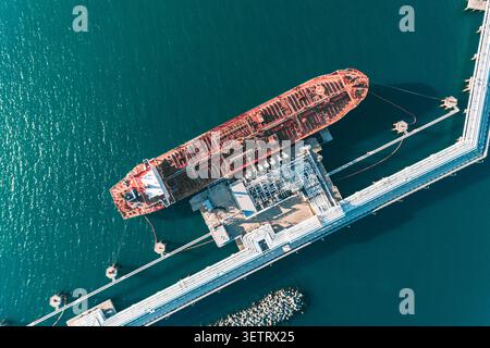 Veduta aerea dall'alto verso il basso di una grande petroliera ancorata a un molo del porto in fase di carico. Foto Stock