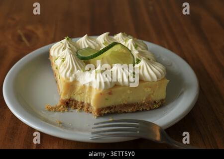 Parzialmente mangiata fetta di crostata al lime con forchetta su piatto bianco Foto Stock